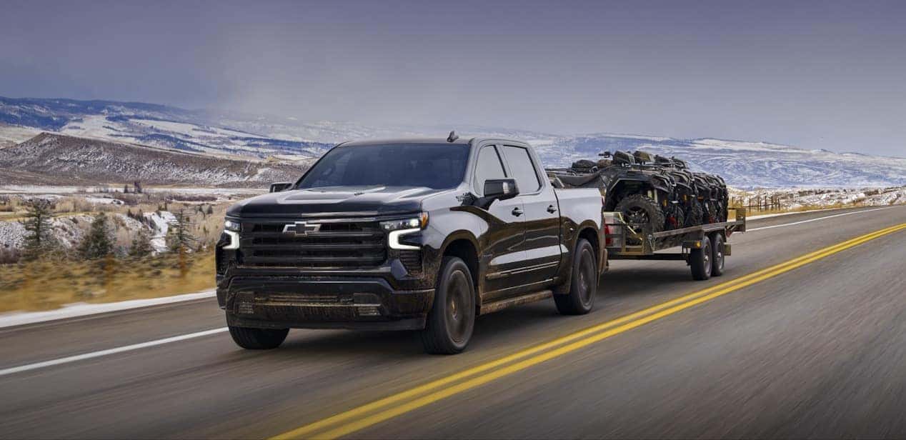 2024 Chevy Silverado in black pulling a trailer next to a vast hilly landscape