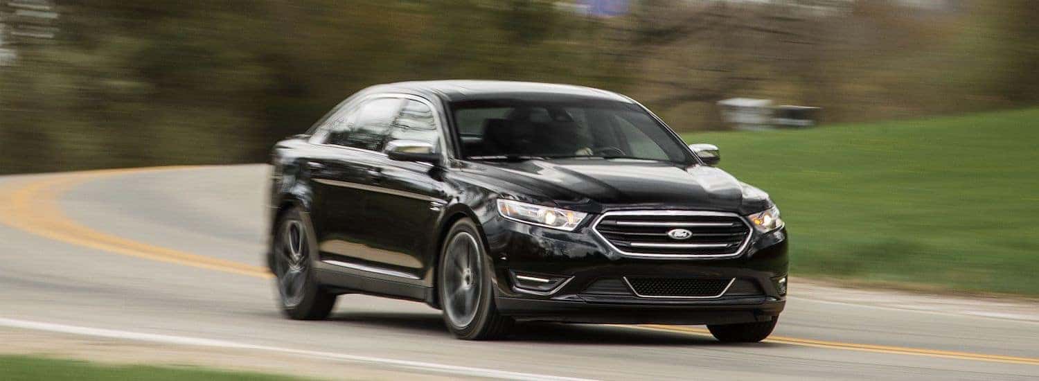 A used black 2015 Ford Taurus drives an empty road outside Atlanta