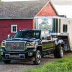 A black 2017 GMC Sierra Denali 3500HD towing a trailer in front of a barn