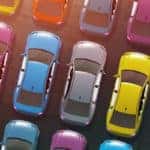 a colorful rainbow lineup of red, blue, yellow, purple, silver, and more colored cars parked together on a dealership lot