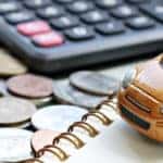 a small gold toy car set up next to a calculator, notebook, and jar of coins for calculating car financing