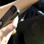 a driver texting on their cellphone as the turn the steering wheel on a road