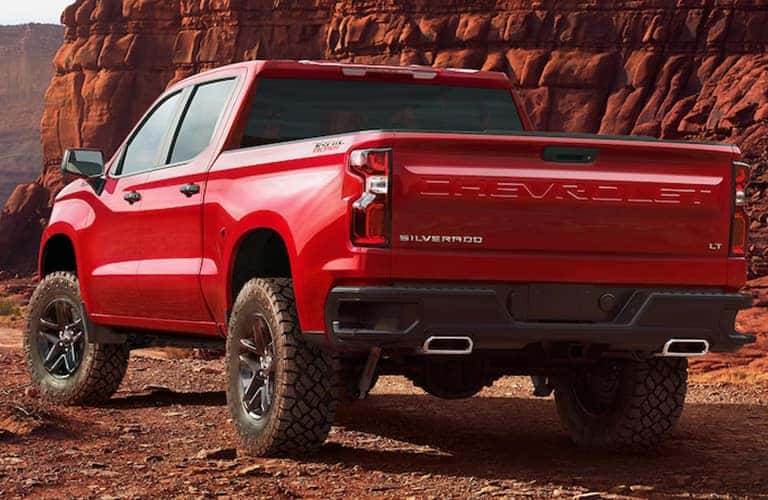 2019 Chevy Silverado exterior rear shot with red paint color and model name imprint on truck bed bumper with a red rock mountain background