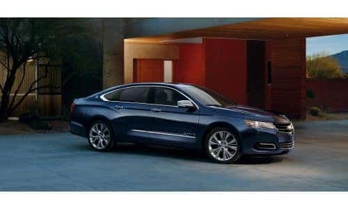 2020 Chevy Impala exterior side shot with dark blue paint color parked outside a luxury home in the evening