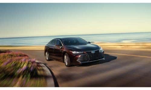 2020 Toyota Avalon exterior shot with red purple paint color driving on a highway near a beach