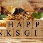Happy Thanksgiving written out in wooden blocks near a cornucopia of leaves, nuts, corn, vegetables, and other autumn and fall assortments