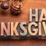 Happy Thanksgiving header in letter block on a wooden table near ornamental acorns and pinecones