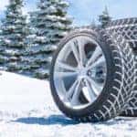 a pile of tires with their tread lined with snow sitting out near sheets of white snow and an evergreen tree forest