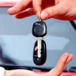 a car delivery salesman handing over the car keys to a new vehicle owner