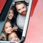 a family looking through a moonroof built into the roof of a red car