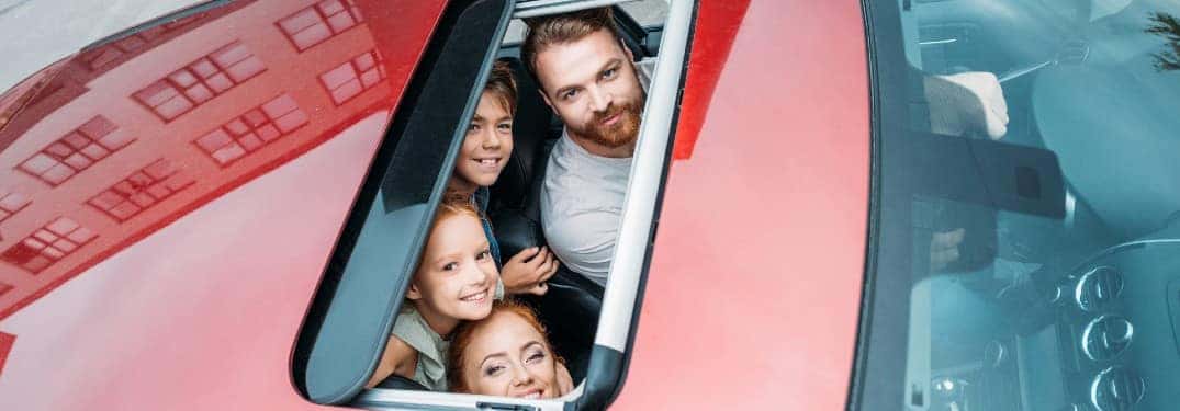 a family looking through a moonroof built into the roof of a red car