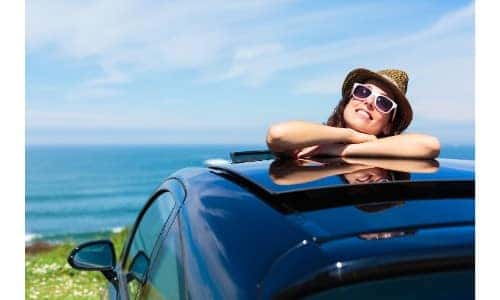 woman relaxing on top of car through an open sunroof on a grassy hill by the water