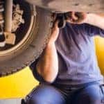 an auto mechanic in a blue jumpsuit fixing a tire on a lifted car in an auto service shop