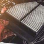 Car cabin air filter replacement being shown next to an open car hood by a service technician