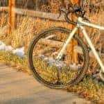 a touring bike with a white frame parked on a bike trail and leaning against a wooden fence