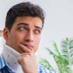 a young man sitting on a couch with a neck brace and thinking