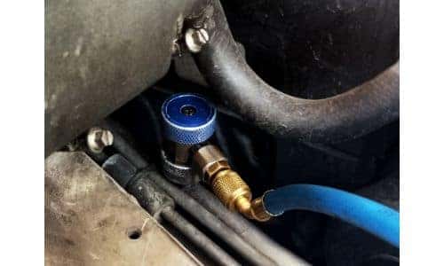 a closeup shot of a refrigerant recharge nozzel and hose attached to a vehicle