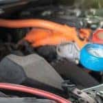 a mechanic operating the gauges on an air conditioner recharger and hose under the hood of a vehicle