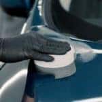 a gloved hand polishing the top of a blue car