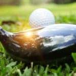 a golf club set up to a golf tee and golf club on the green and the sun reflects off of it