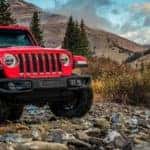2020 Jeep Wrangler Rubicon exterior shot with Firecracker Red paint color parked on rocks next to a creek