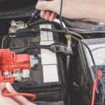 a service mechanic working on charging a car's battery under the hood