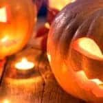 carved and lit jack-o'-lantern pumpkins on a wooden table surrounded by fall leaves and candles