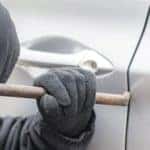 a man in a hoodie and gloves breaking into a car using a crowbar