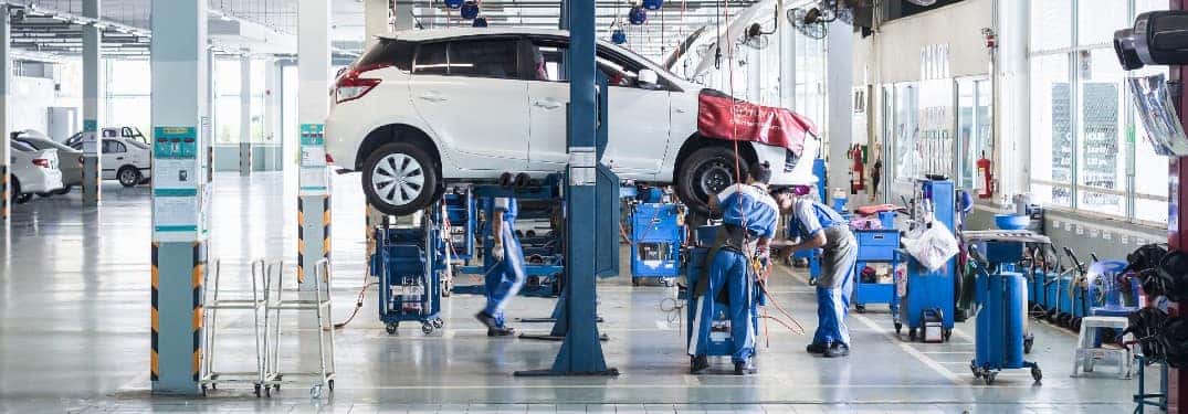 a group of service technicians and mechanics working on a white SUV in a service garage