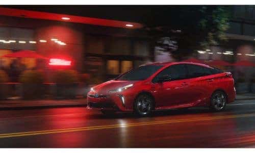 2021 Toyota Prius 2020 Edition exterior shot with red paint color driving through a city downtown at night