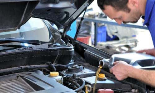 a service team member adding fresh oil to a vehicle under its propped car hood
