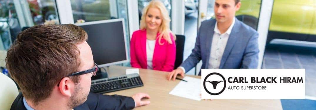 Car Salesman Talking with a Couple at a Desk with Carl Black Hiram Logo