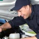 a smiling man looking under a car's hood
