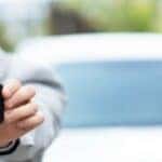 a person holding keys and standing in front of a white car