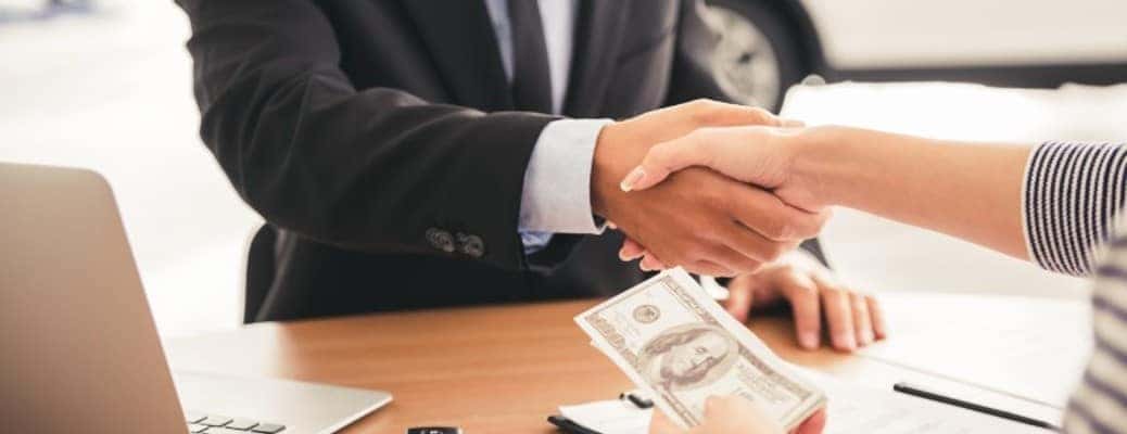 A handshake over a table with a dollar bill being passed