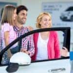 three people and a child standing by the open door of a white car