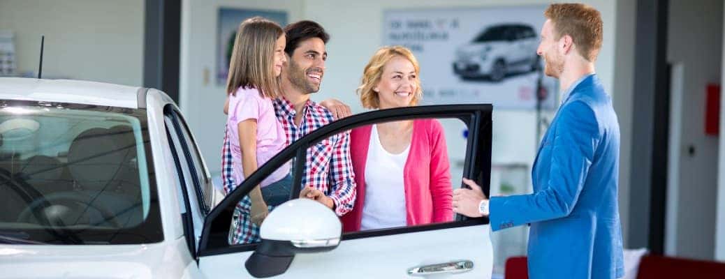 three people and a child standing by the open door of a white car
