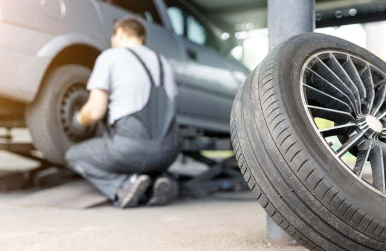 a man crouching by a car replacing a tire