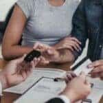 three people at a table passing keys and a credit card between them