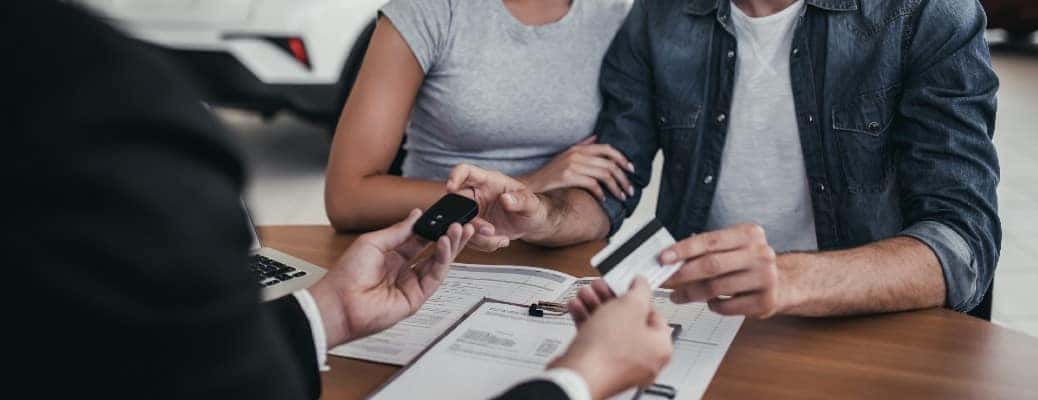 three people at a table passing keys and a credit card between them