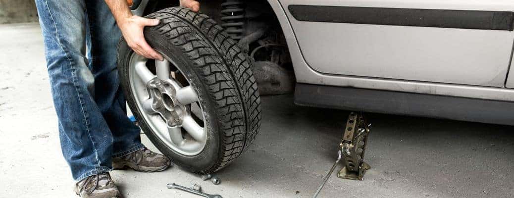 a person holding a car tire by a car