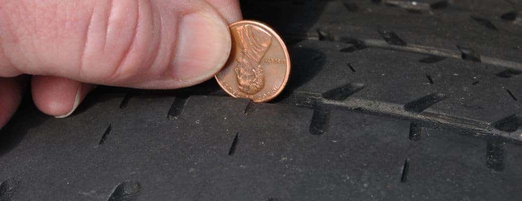 fingers holding a penny to a car tire