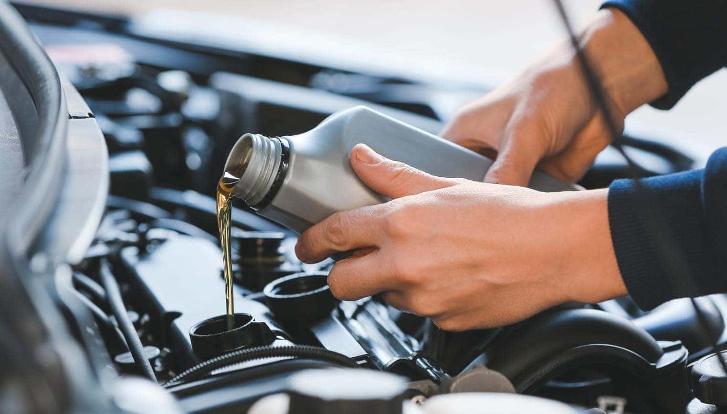 A close-up of hands pouring fresh motor oil from a container into a vehicle’s engine during an oil change.