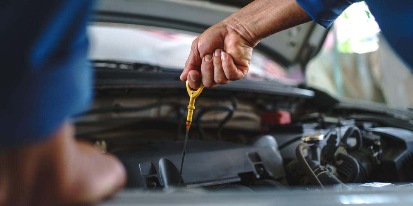 A close-up of a technician checking a vehicle’s engine oil level with the dipstick under an open hood.