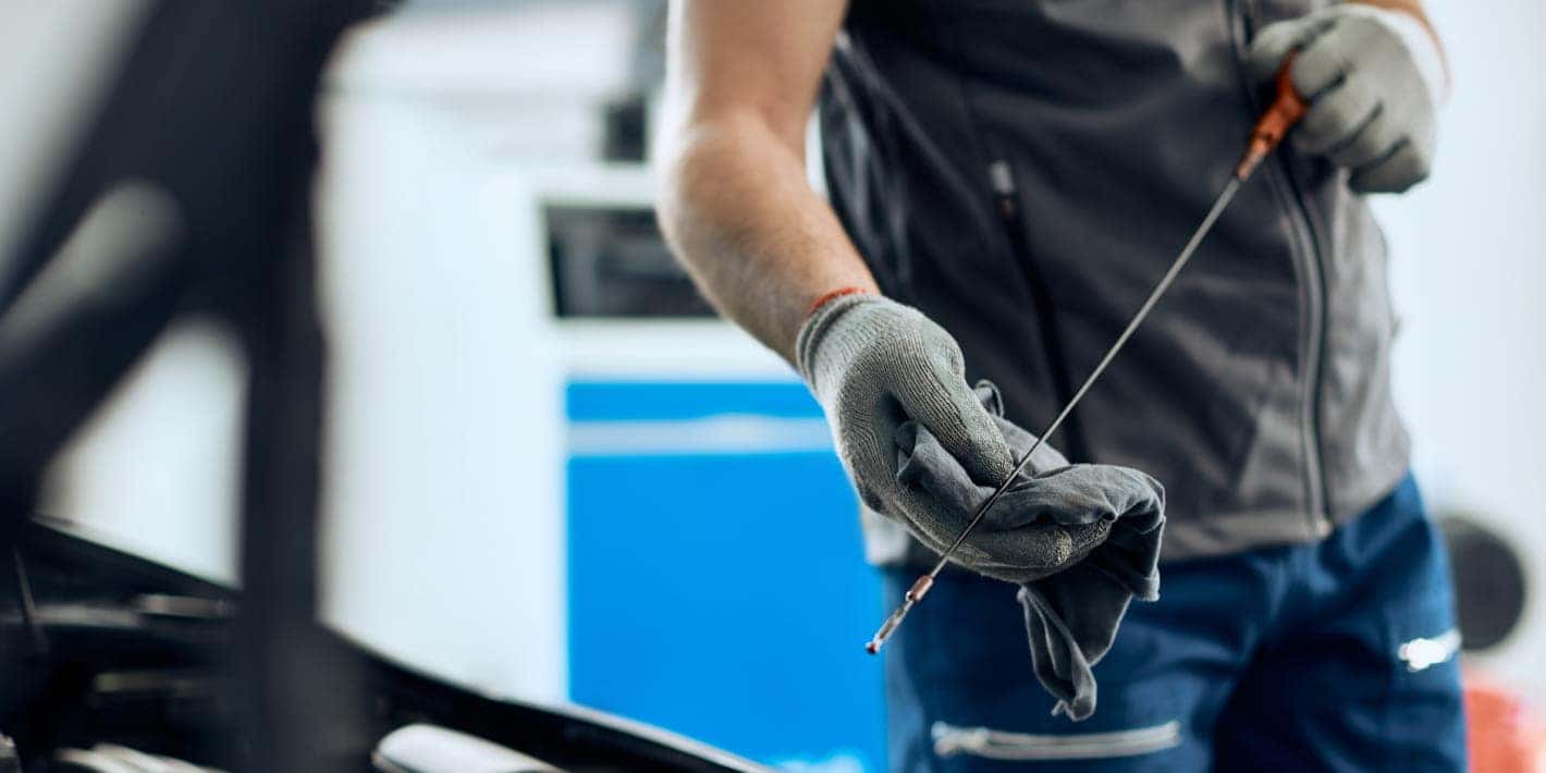 Technician wearing protective gloves wiping an engine oil dipstick with a cloth during a vehicle oil inspection.