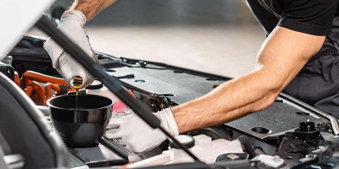A technician wearing protective gloves pours fresh motor oil into a vehicle’s engine using a funnel.