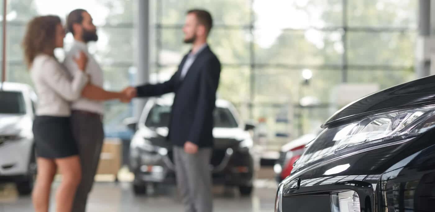 Customer shakes hands with a dealership salesperson beside vehicles in a showroom.