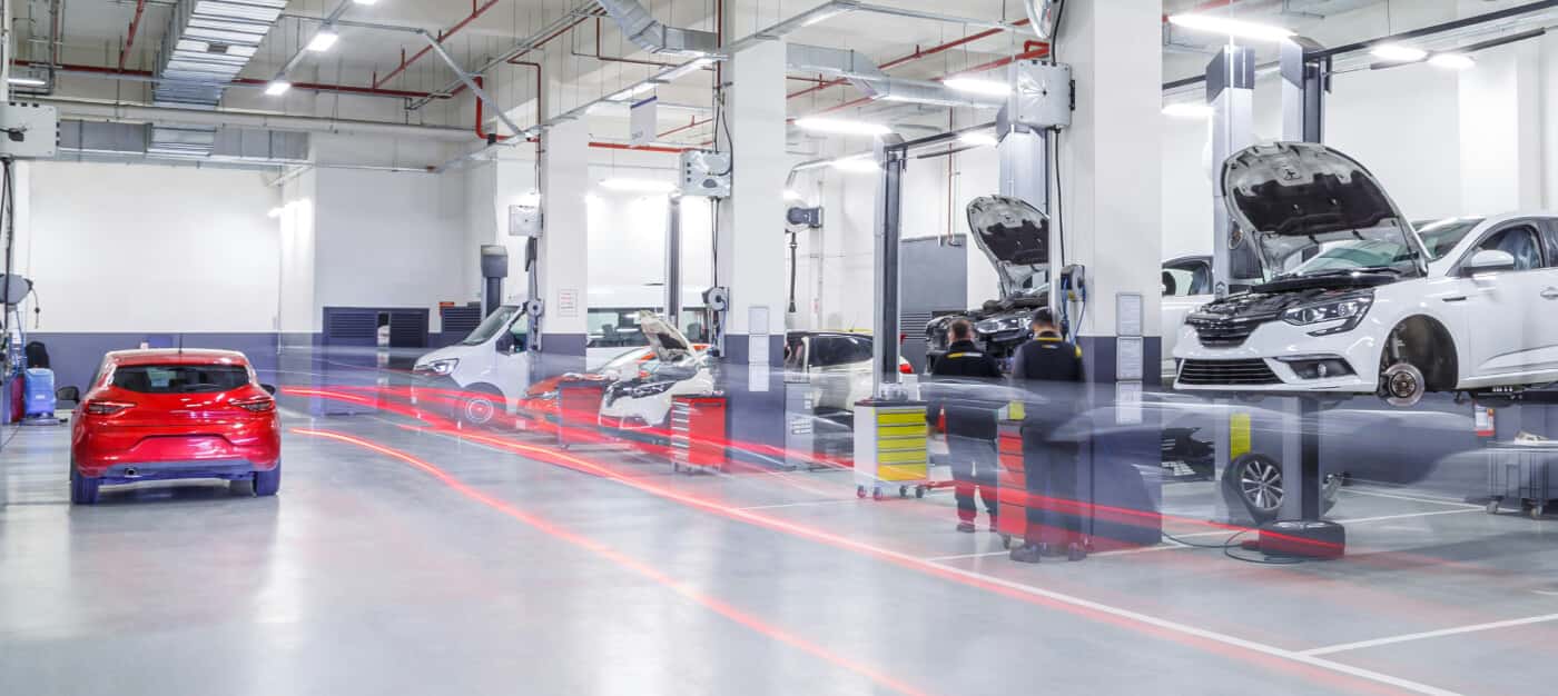 Automotive technicians service multiple vehicles in a bright dealership repair bay.
