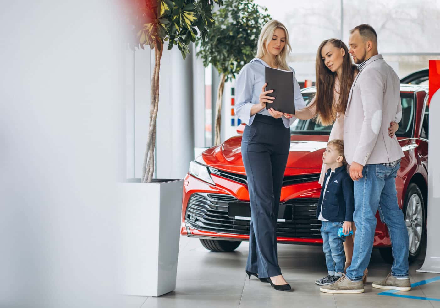 Dealership salesperson reviews vehicle options with a family beside a red SUV in the showroom.