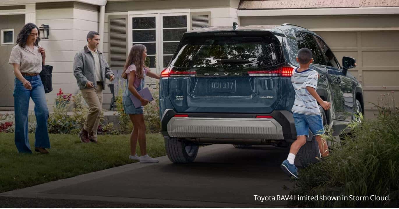 Rear view of a Storm Cloud Toyota RAV4 Limited as a family approaches the vehicle in a suburban driveway.